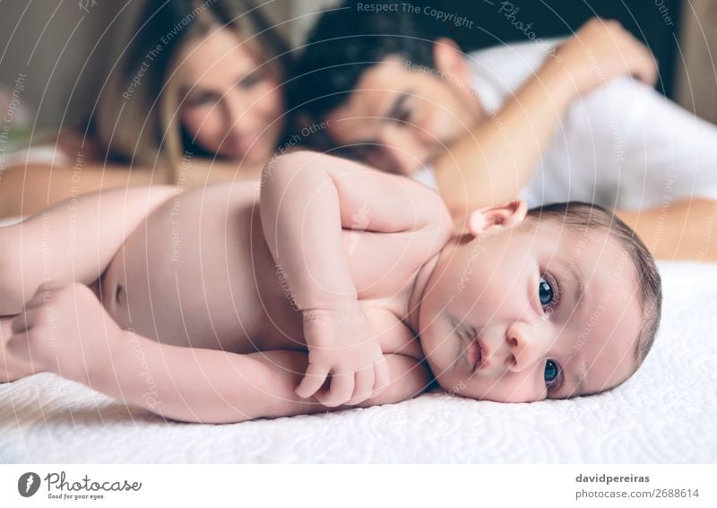 Neugeborenes liegt über dem Bett und das Paar lächelt auf dem Hintergrund. Lifestyle Freude Glück schön Freizeit & Hobby Schlafzimmer Kind Mensch Baby Kleinkind