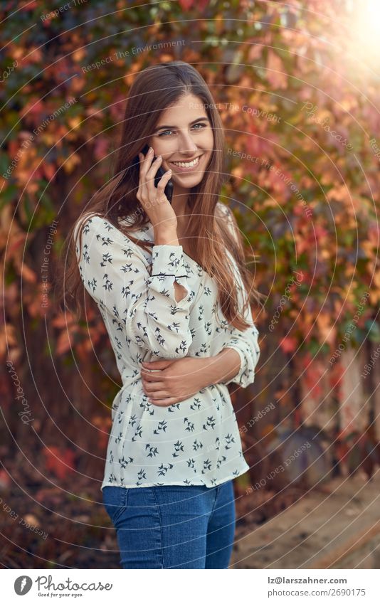 Lächelnde junge Frau, die im Herbst auf einem Handy plaudert. Glück Gesicht Sommer Business Telefon PDA Erwachsene 1 Mensch 18-30 Jahre Jugendliche Blatt Straße