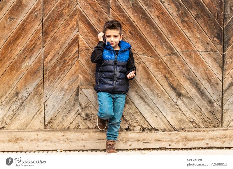 Kleiner Junge mit einem beweglichen Telefon mit einem Hintergrund aus Holztüren. Lifestyle Stil Design schön Spielen Ferien & Urlaub & Reisen Winter Haus