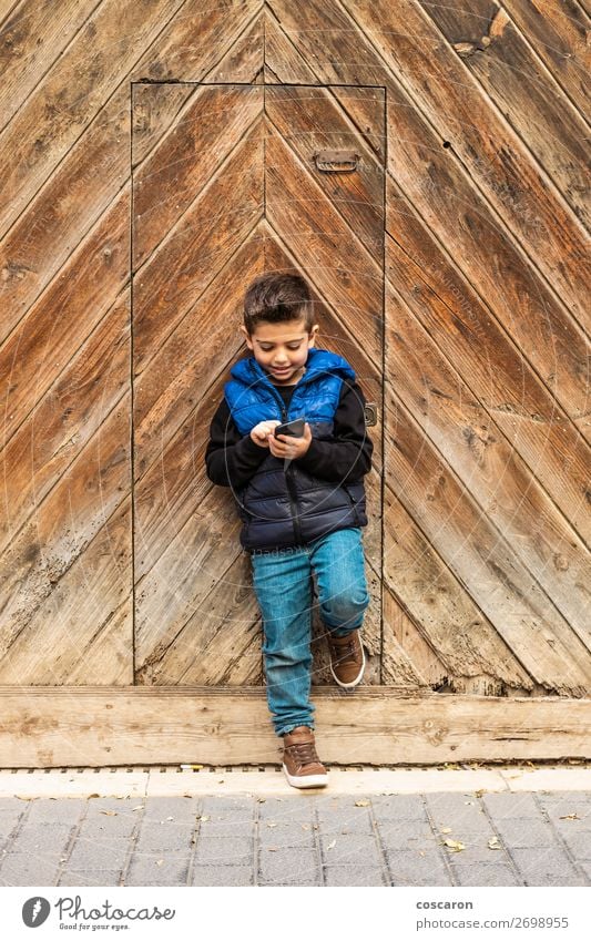 Kleiner Junge mit einem beweglichen Telefon mit einem Hintergrund aus Holztüren. Lifestyle Design schön Spielen Ferien & Urlaub & Reisen Haus Kind Handy PDA