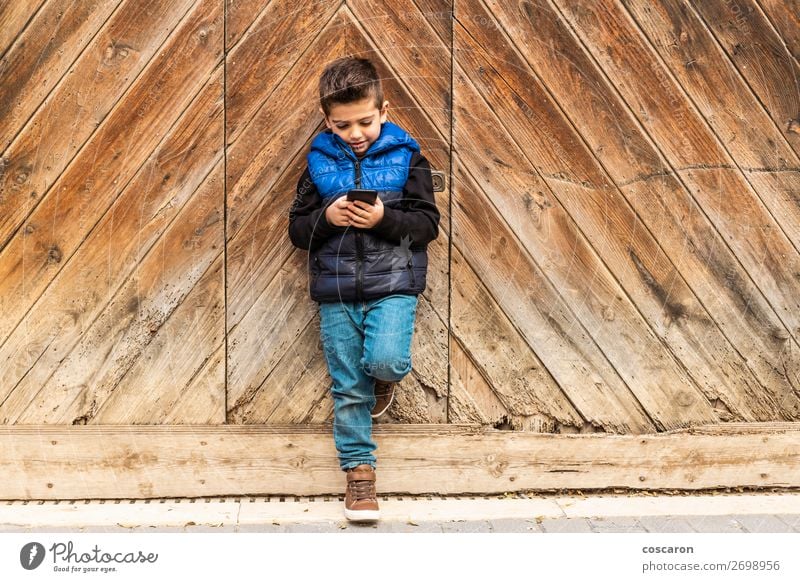 Kleiner Junge mit einem beweglichen Telefon mit einem Hintergrund aus Holztüren. schön Spielen Ferien & Urlaub & Reisen Haus Kind Handy PDA