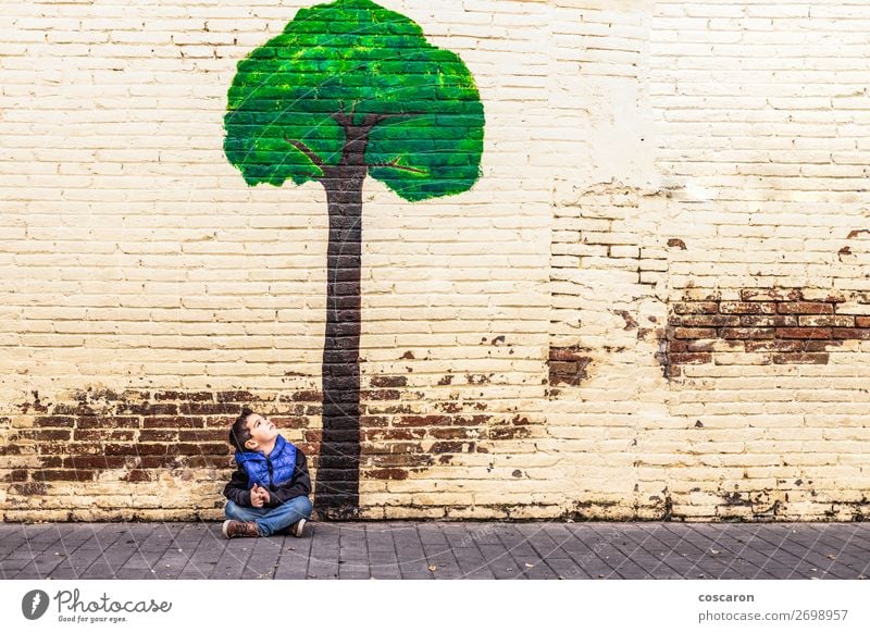 Kleines Kind, das unter einem Baum sitzt, der an einer Wand gemalt ist. Freude Glück schön Spielen Ferien & Urlaub & Reisen Tourismus Abenteuer Sommer Garten