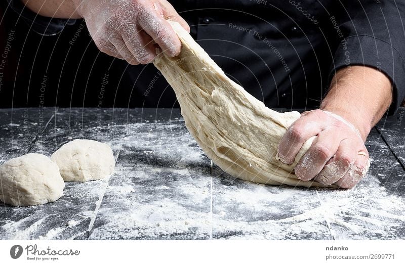 Chefkoch in schwarzer Uniform kneten weißes Weizenmehl Teigwaren Backwaren Brot Ernährung Tisch Küche Koch Mensch Mann Erwachsene Hand Holz machen frisch