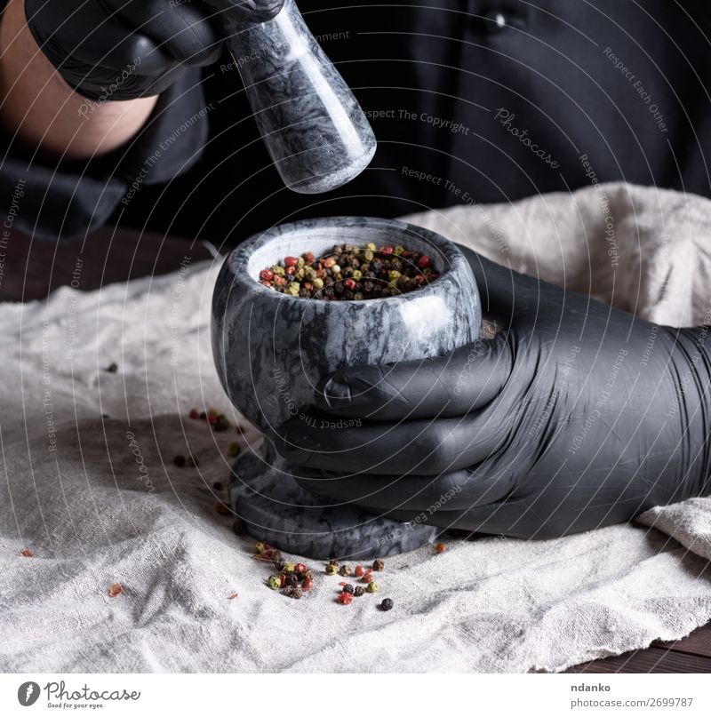 in schwarzen Latexhandschuhen kochen, die einen Steinmörser mit Pfeffer halten. Kräuter & Gewürze Schalen & Schüsseln Tisch Küche Arbeit & Erwerbstätigkeit Koch