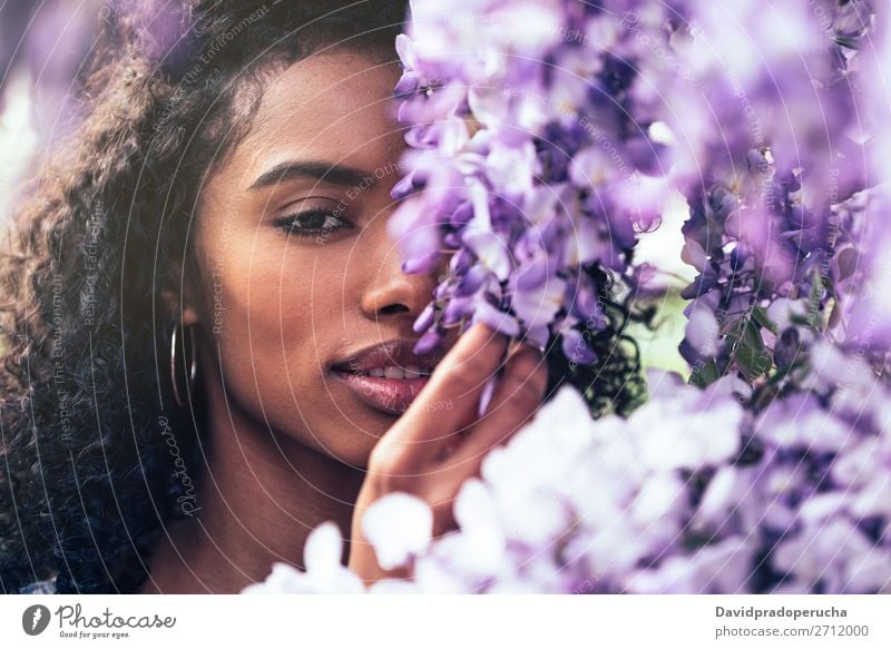 Nachdenklich fröhliche junge schwarze Frau, umgeben von Blumen. Blüte Frühling Fliederbusch Nahaufnahme multiethnisch Afrikanisch Person gemischter Abstammung