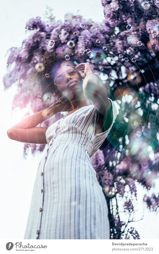 Fröhliche junge schwarze Frau, umgeben von Blumen. Blüte Frühling Fliederbusch Porträt multiethnisch Afrikanisch Person gemischter Abstammung Lächeln Wegsehen