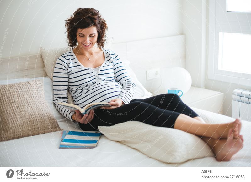 Glückliche schwangere Frau beim Lesen auf dem Bett schön Körper Erholung Freizeit & Hobby lesen Schlafzimmer Baby Erwachsene Eltern Mutter Buch sitzen Zukunft