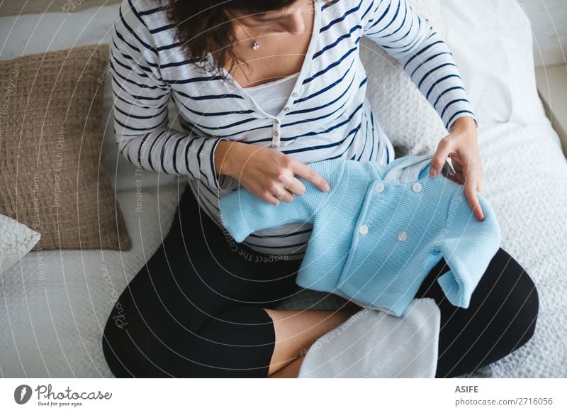 Schwangere Frau beim Vorbereiten der Babykleidung Glück Körper Erholung Freizeit & Hobby Junge Erwachsene Eltern Mutter Bekleidung Pullover sitzen klein