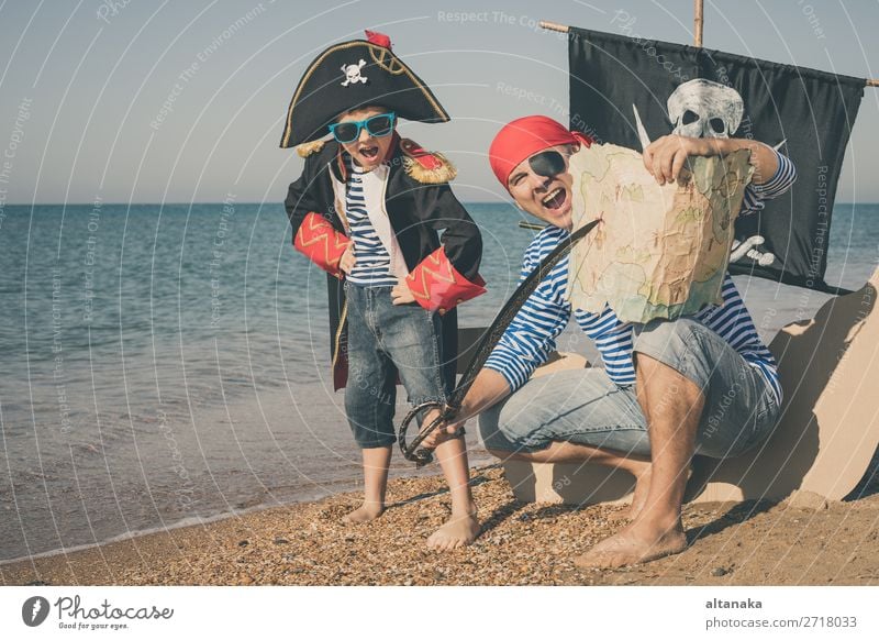 Vater und Sohn spielen zur Tageszeit am Strand. Sie sind mit Matrosenwesten und Piratenkostümen bekleidet. Konzept des glücklichen Spiels im Urlaub und der freundlichen Familie.