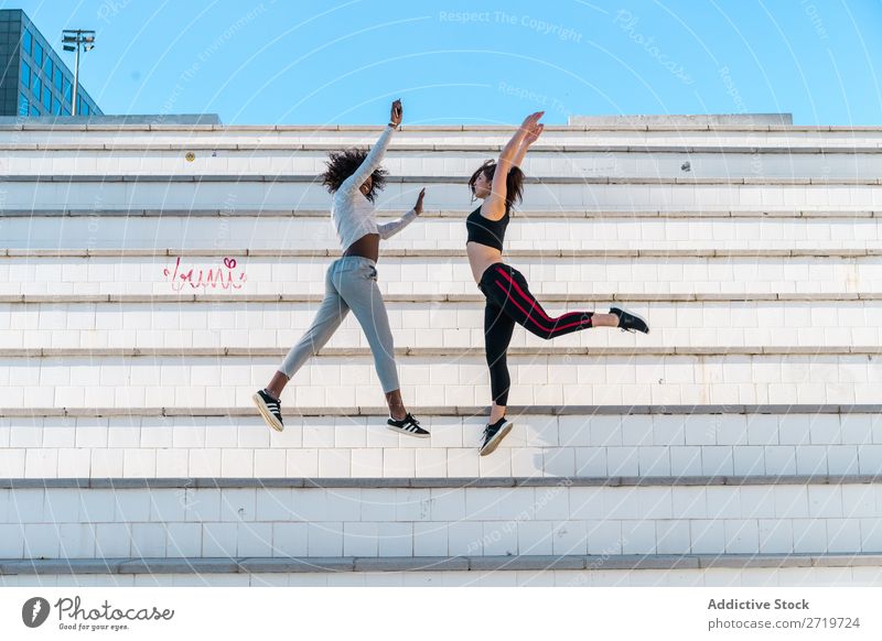 Hübsche, fitte Frauen, die zusammen springen. sportlich Zusammensein hübsch Jugendliche heiter Lächeln Freitreppe strecken schön Sport multiethnisch