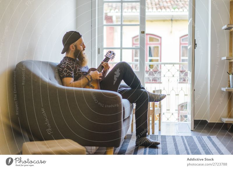 Mann spielt Gitarre im Sessel heimwärts Erholung Erwachsene bärtig sitzen Spielen Musiker akustisch lässig Jugendliche Haus Lifestyle Raum gutaussehend Leben