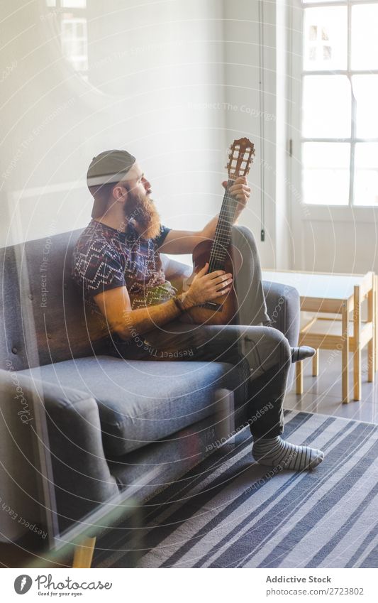 Mann spielt Gitarre im Sessel heimwärts Erholung Erwachsene bärtig sitzen Spielen Musiker akustisch lässig Jugendliche Haus Lifestyle Raum gutaussehend Leben