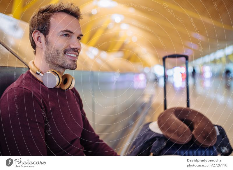 Junger Mann, der am Flughafen mit einem Koffer auf Musik hört und das Handy benutzt. warten Jugendliche Lächeln Kaukasier hören Kopfhörer blond Etage Business