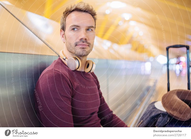 Junger Mann, der am Flughafen mit einem Koffer auf Musik hört und das Handy benutzt. warten Jugendliche Lächeln Kaukasier hören Kopfhörer blond Etage Business