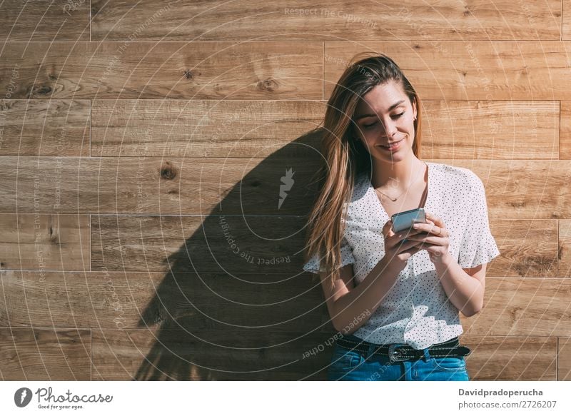 Glückliche Frau mit Smartphone an einer Holzwand PDA Telefon Mobile Mitteilung Gerät Lächeln Wegsehen Porträt Hintergrundbild Sommer Wand Halt klug Jugendliche