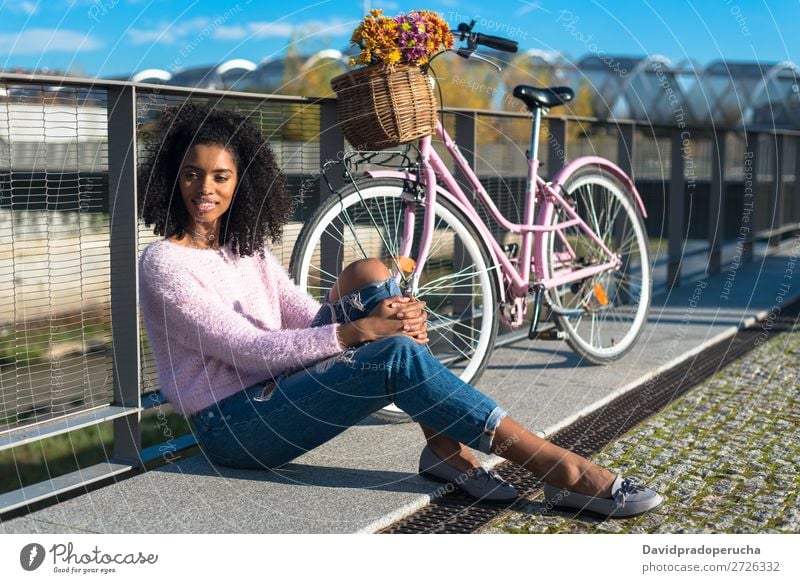 Schwarze junge Frau sitzt mit ihrem alten Fahrrad am Fluss. Mädchen schön retro Blume Glück altehrwürdig Blumenstrauß rosa Sommer Jugendliche hübsch Frühling