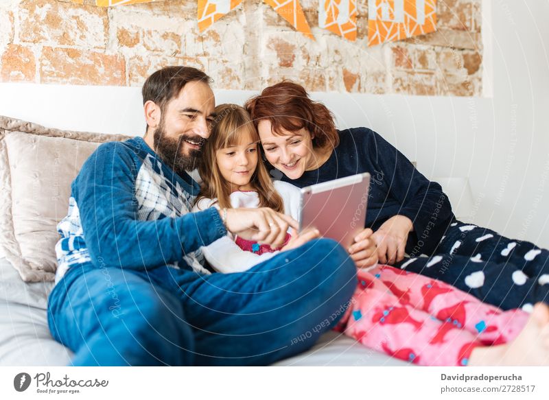 Ein Paar entspannt zu Hause im Bett mit seiner kleinen Tochter auf dem Handy und Tablett. Zuneigung Schlafzimmer Ehefrau Ehemann Kind Mobile Telefon