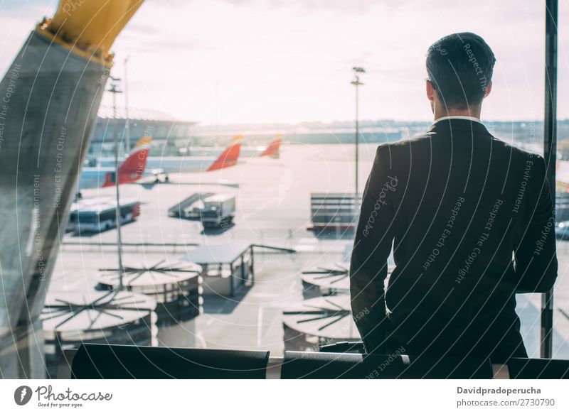 Zurück von einem jungen Geschäftsmann, der mit dem Koffer am Flughafen steht und auf den Flug wartet. Mann Ferien & Urlaub & Reisen Schatten Rücken Business