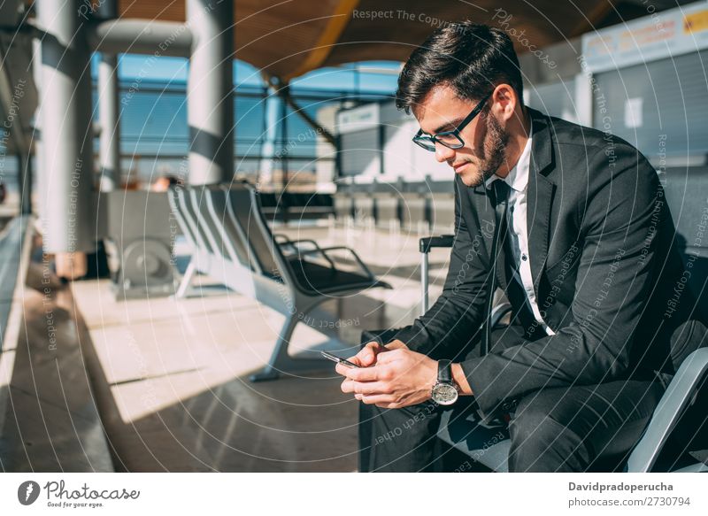 Junger Geschäftsmann am Telefon mit dem Koffer am Flughafen, der auf den Flug wartet. Mann Ferien & Urlaub & Reisen Mobile Mitteilung Technik & Technologie