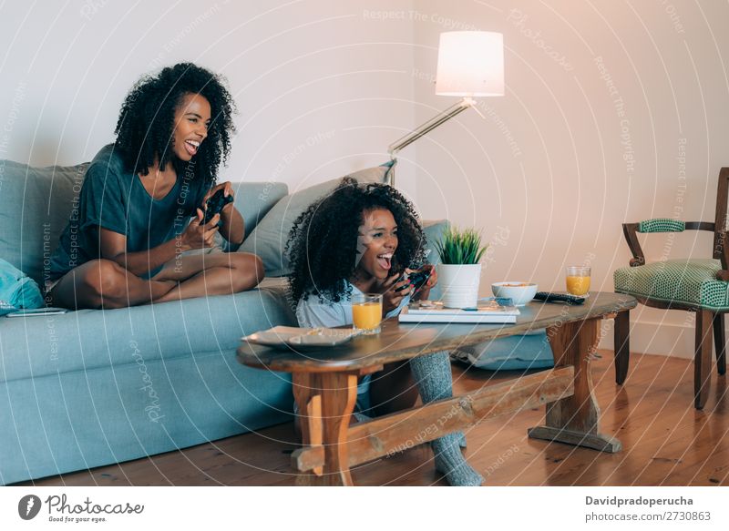 Glückliche junge zwei schwarze Frauen, die auf der Couch sitzen und Videospiele spielen. Konsole Spielen Technik & Technologie modernes Verhältnis heimwärts