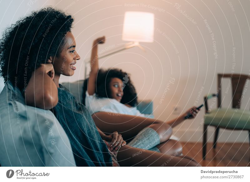 Glückliche junge zwei schwarze Frauen liegen auf der Couch und schauen fern. Fernsehen Technik & Technologie beobachten modernes Verhältnis heimwärts