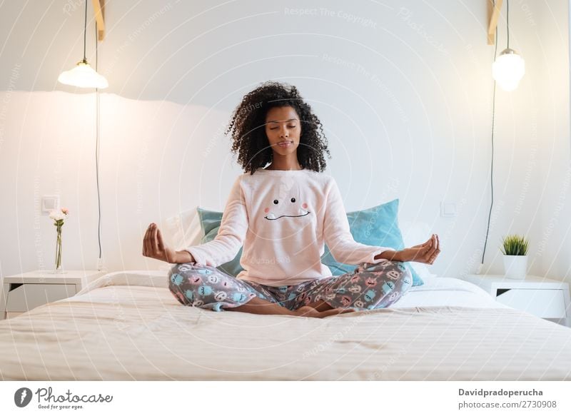 Glückliche, schöne, junge, schwarze Frau, die sich zu Hause entspannt und die Morgenmeditation im Bett macht. Yoga Meditation Verstand Schlafanzug Pyjama üben