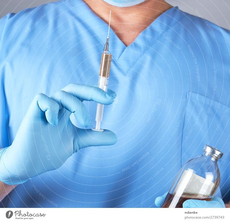 männlicher Arzt in blauer Uniform, der eine Spritze hält. Gesundheitswesen Behandlung Krankenpflege Krankheit Medikament Wissenschaften Labor Krankenhaus Mensch