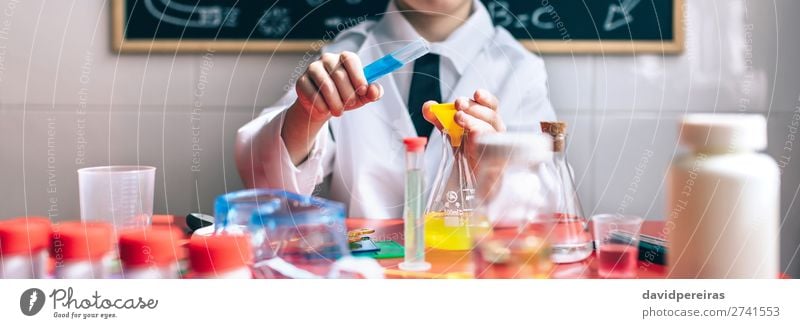 Ernsthafter kleiner Junge beim Spielen mit chemischen Flüssigkeiten Flasche Glück Tisch Wissenschaften Kind Klassenraum Tafel Labor Internet Mensch Kindheit