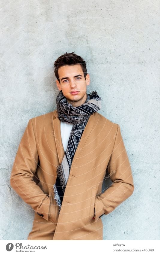Trendy junger Mann mit Mantel und Schal, der sich an eine Wand lehnt. Lifestyle elegant Stil schön Haare & Frisuren Mensch maskulin Junger Mann Jugendliche