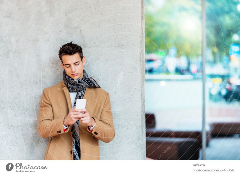 Stilvoller junger Mann in Denimkleidung, der sich an eine Wand lehnt. Lifestyle elegant schön Haare & Frisuren Telefon PDA Junger Mann Jugendliche Erwachsene