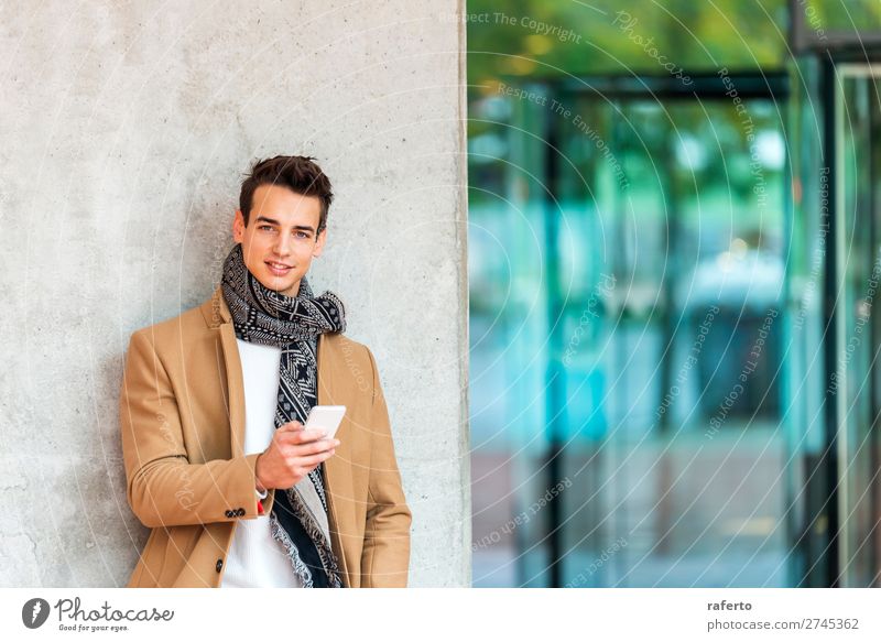junger Mann in Jeanskleidung, der sich an eine Wand lehnt, während er im Freien ein Mobiltelefon benutzt Lifestyle elegant Stil schön Haare & Frisuren Telefon