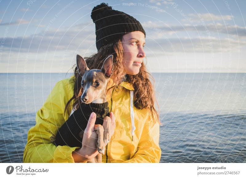 Frau mit ihrem kleinen Hund am Strand Lifestyle Ausflug Freiheit Sonne Winter Freundschaft 30-45 Jahre Erwachsene Natur Tier Horizont Küste Jacke Mantel Hut