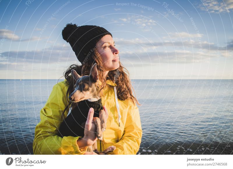 Frau mit ihrem kleinen Hund am Strand Lifestyle Erholung Ausflug Freiheit Sonne Winter 30-45 Jahre Erwachsene Natur Tier Horizont Küste Jacke Mantel Hut