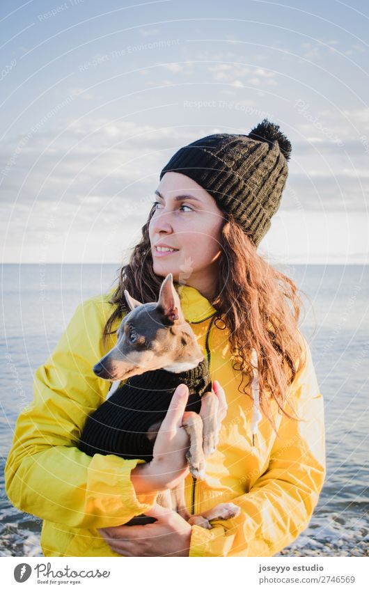 Frau mit ihrem kleinen Hund am Strand Lifestyle Erholung Ausflug Freiheit Sonne Winter Freundschaft 30-45 Jahre Erwachsene Natur Tier Horizont Küste Jacke