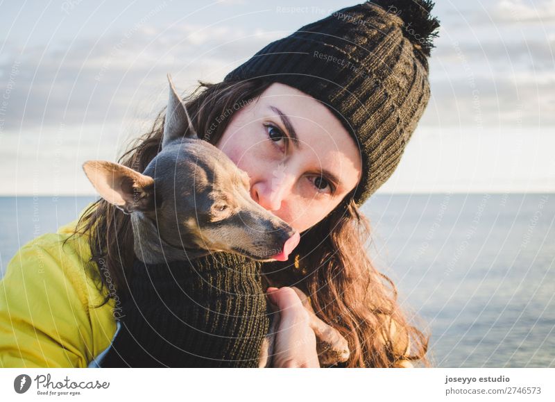 Frau mit ihrem Hund am Strand Lifestyle Erholung Ausflug Freiheit Sonne Winter Freundschaft 30-45 Jahre Erwachsene Natur Tier Horizont Küste Jacke Mantel Hut