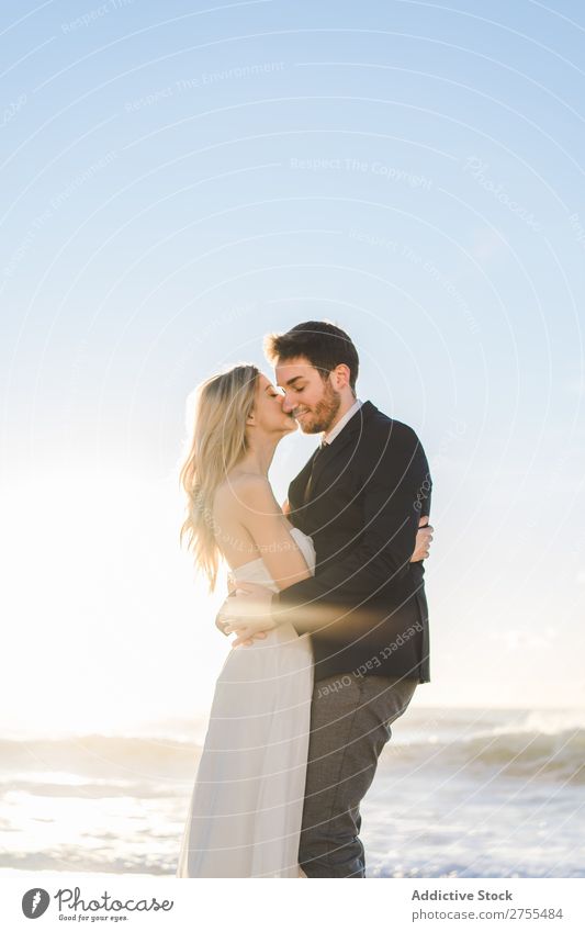 Zärtlich küssendes Brautpaar im Sonnenlicht Paar Hochzeit Strand umarmend Engagement Zufriedenheit Valentinsgruß Genuss verliebt Meereslandschaft stehen