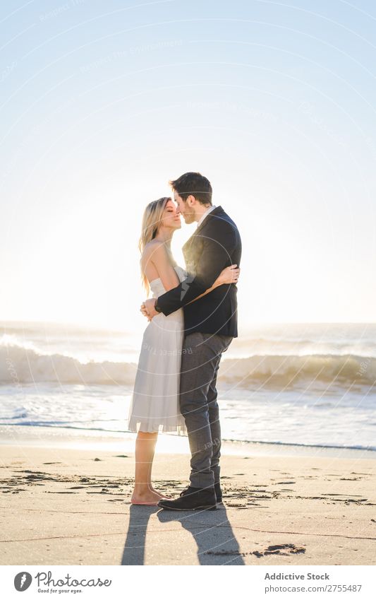 Zärtlich küssendes Brautpaar im Sonnenlicht Paar Hochzeit Strand umarmend Engagement Zufriedenheit Valentinsgruß Genuss verliebt Meereslandschaft stehen