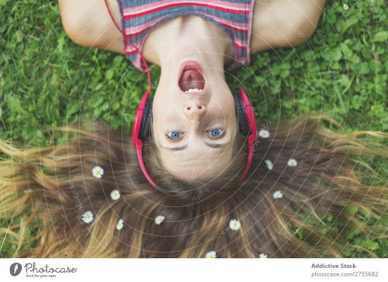 Aufgeregtes Mädchen in Kopfhörern auf Gras Frau expressiv Körperhaltung lügen Park Gesichtsbehandlung Blume Aufregung Model Mund geöffnet Ausdruck Stil