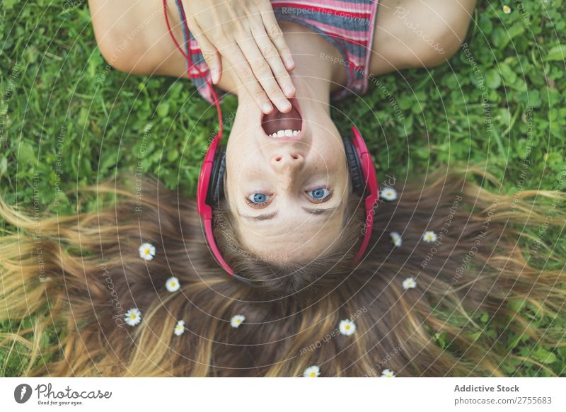 Aufgeregtes Mädchen in Kopfhörern auf Gras Frau expressiv Körperhaltung lügen Park Gesichtsbehandlung Blume Aufregung Model Mund geöffnet Ausdruck Stil