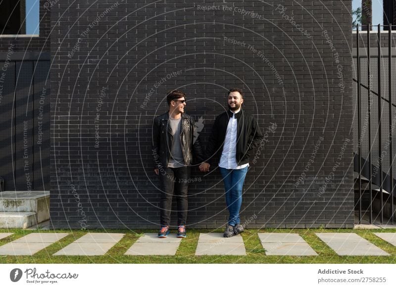 Alternatives Paar an der Ziegelmauer Stehen Wand Baustein Händchenhalten in die Kamera schauen posierend schwul Homosexualität männlich Liebe zwei Zusammensein
