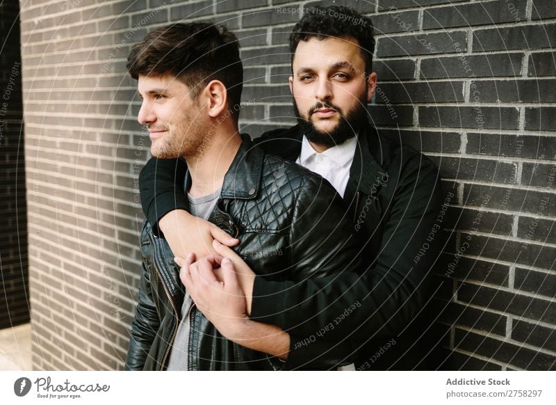 Schwules Paar umarmt sich in der Nähe einer Ziegelmauer schwul Umarmen umarmend in die Kamera schauen Glück Stehen Wand Baustein posierend Homosexualität