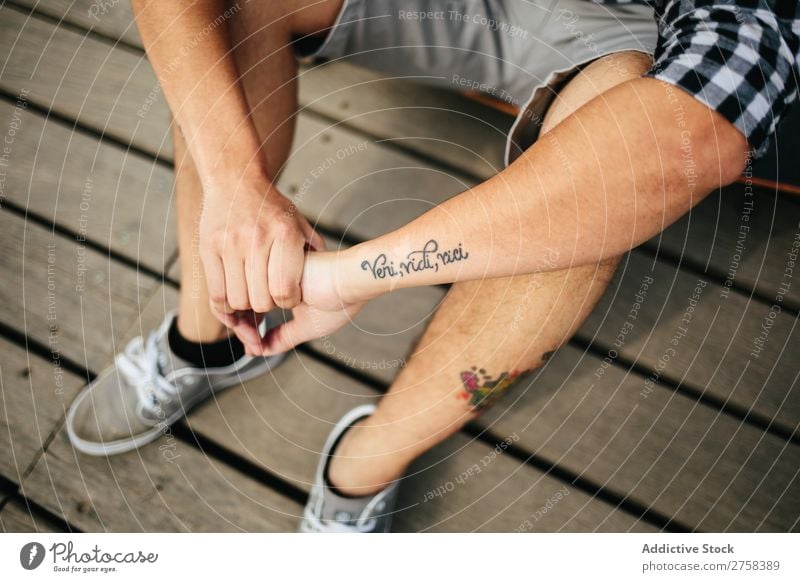 Mann mit Tattoos auf Holzboden sitzend tätowiert Shorts Lifestyle Jugendliche attraktiv Turnschuh Outfit Etage anonym unkenntlich Typ lässig Pose Nahaufnahme
