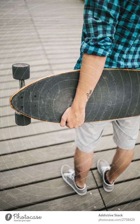 Mann mit Tattoos, der Skateboard an Land hält. Rückansicht. Küste Strand Freizeit & Hobby Sommer mehrfarbig Youngster Aktion Jugendliche Sport Schlittschuhe