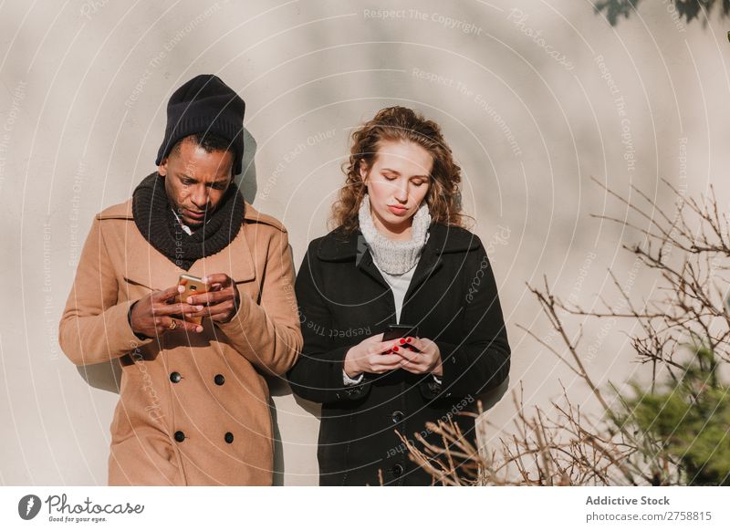 Paar in warmer Kleidung mit Smartphones multiethnisch Stil Straße warme Kleidung PDA benutzend stehen lässig schön Person gemischter Abstammung schwarz