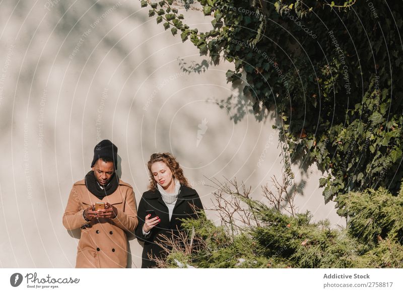 Paar in warmer Kleidung mit Smartphones multiethnisch Stil Straße warme Kleidung PDA benutzend stehen lässig schön Person gemischter Abstammung schwarz