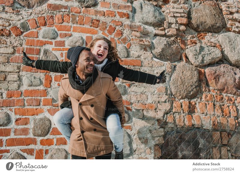 Paar hat Spaß an der Ziegelwand multiethnisch Stil Straße warme Kleidung lässig Backstein Wand tragen auf der Rückseite Stein Huckepack schön