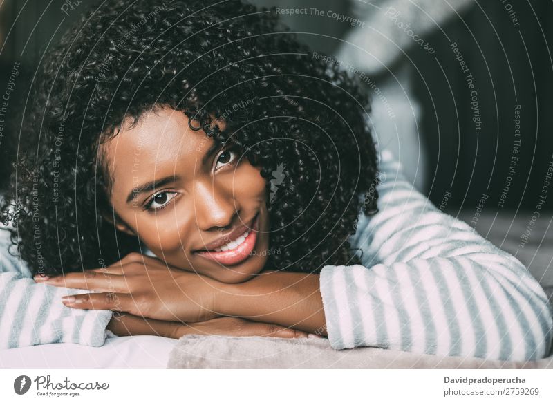 Nahaufnahme einer hübschen schwarzen Frau mit lockigem Haar, die lächelt und auf dem Bett liegt und auf die Kamera schaut. schwarze Frau Porträt lügen Lächeln