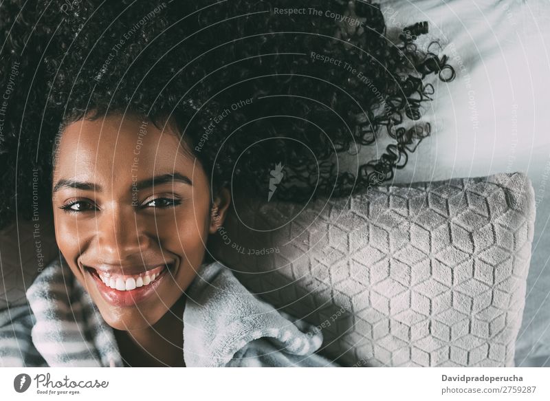 Schöne schwarze Frau mit lockigem Haar, die lächelt und auf dem Bett liegt und auf die Kamera schaut. Lächeln Afrikanisch hübsch schön Vogelperspektive