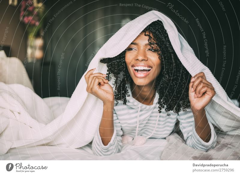 Nahaufnahme einer hübschen schwarzen Frau mit lockigem Haar, die lächelt und mit Laken auf dem Bett bedeckt ist und wegblickt. schwarze Frau Porträt Bettlaken