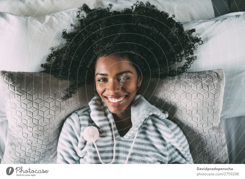 Schöne schwarze Frau mit lockigem Haar, die lächelt und auf dem Bett liegt und auf die Kamera schaut. Lächeln Afrikanisch hübsch schön Vogelperspektive